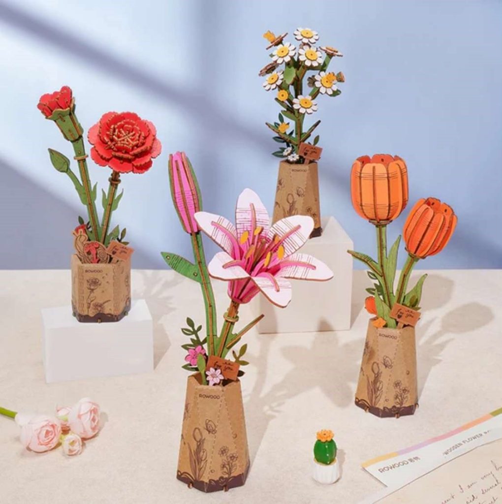 Collection of Robotime 3D wooden puzzle flowers including rose, lily, carnation, chamomile and lilac models in decorative pots