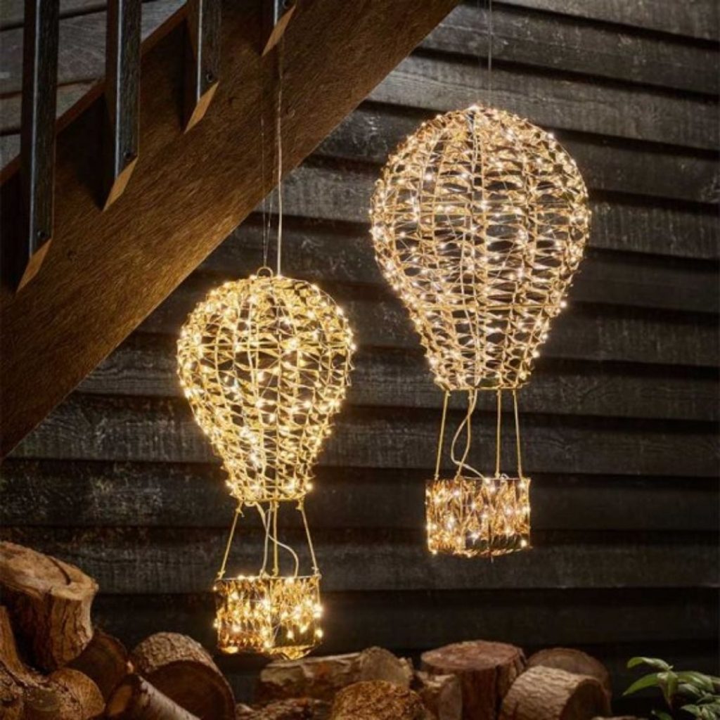 Gold balloon-shaped LED lights hanging by a wooden wall with a warm festive glow.