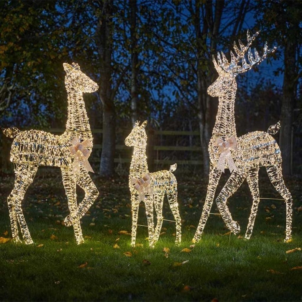 Three illuminated reindeer figures made of twinkling LED lights standing on a lawn at night.