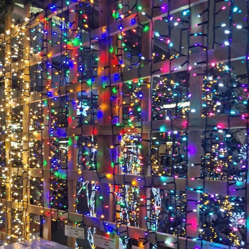 Colourful LED string lights draped along a glass wall, reflecting festive colours.