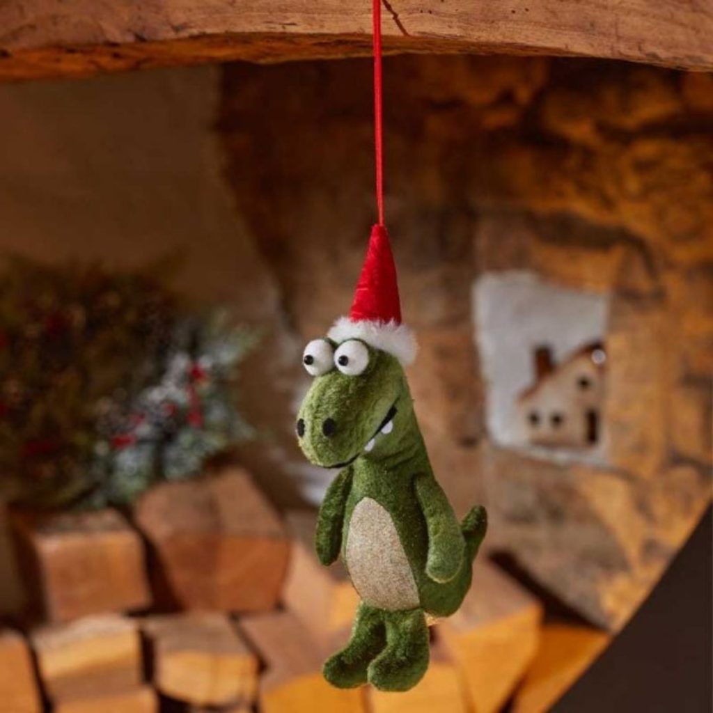 Cute green dinosaur Christmas decoration wearing a red Santa hat, hanging from a branch.